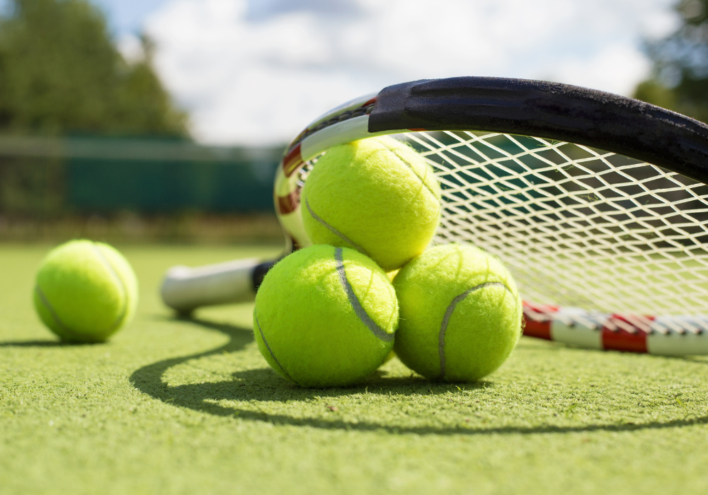 four tennis balls on a grass court with a tennis racket resting on the tennis balls